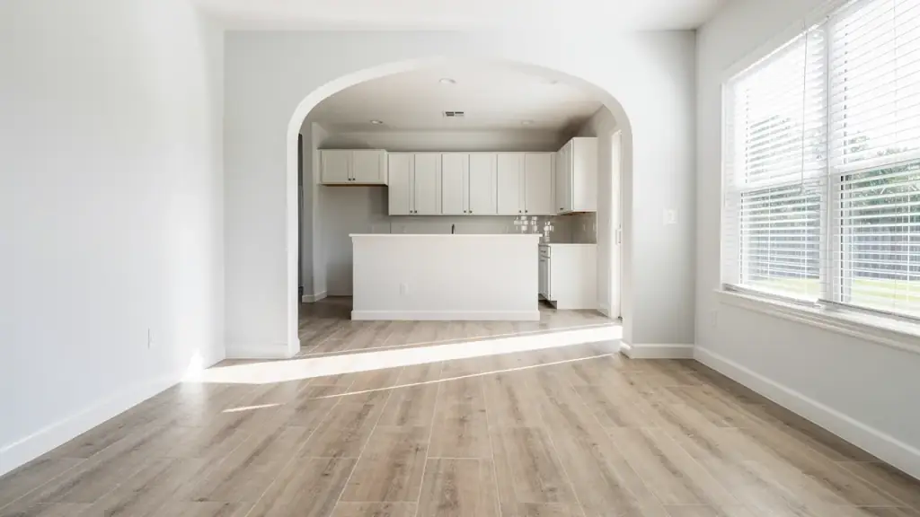 An empty home with clean plank floors, open blinds and an archway through to a wiped kitchen